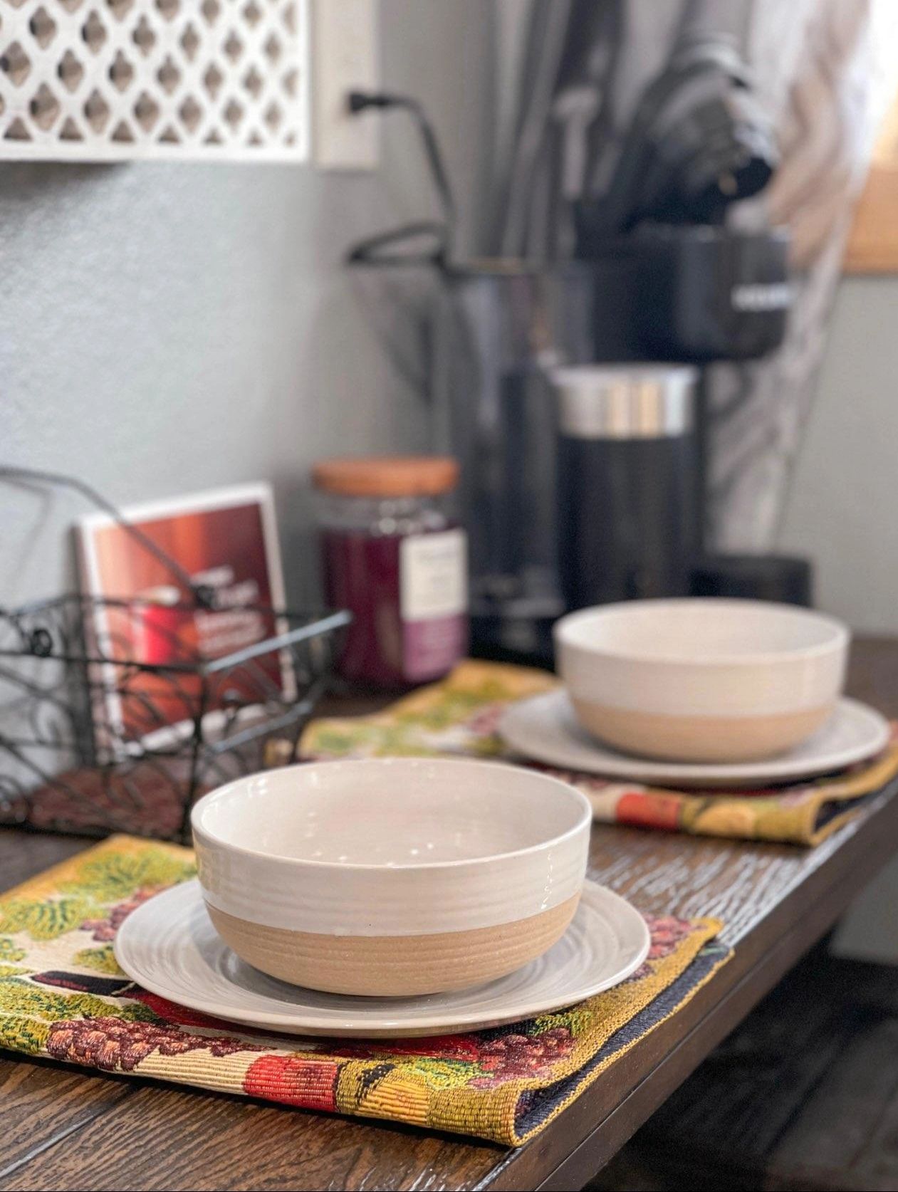 Two bowls on white plates with a colorful cloth underneath on a wooden table.