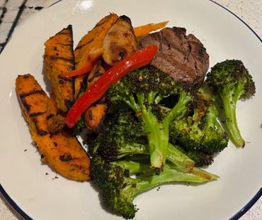 Grilled steak with broccoli, sweet potato, and red pepper on a white plate.