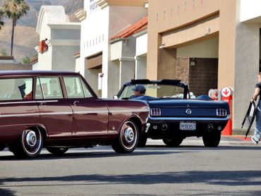Two vintage cars parked near a building with people around.