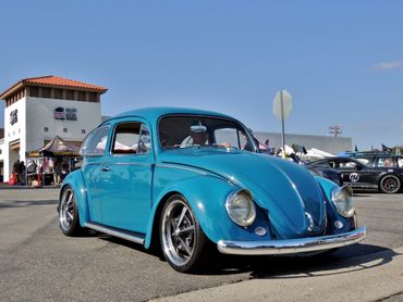 A classic blue Volkswagen Beetle parked at a car show on a sunny day.