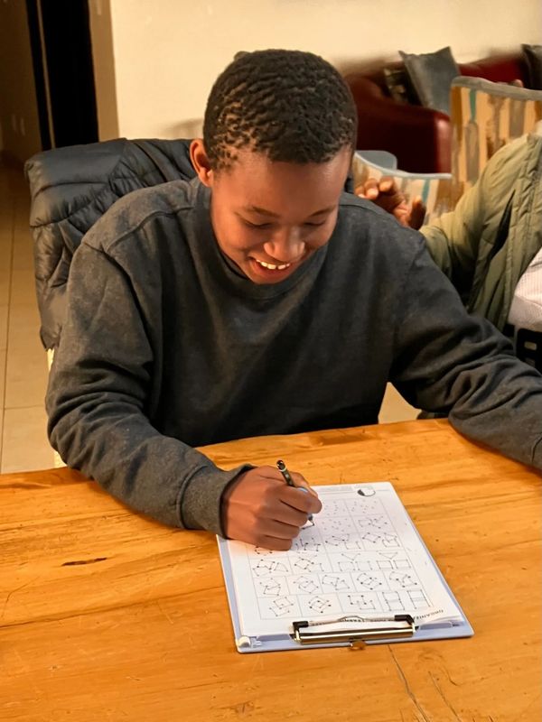 A smiling boy solving puzzles on a clipboard at a wooden table.