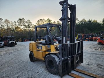 Yellow CAT forklift parked on a gravel lot at sunset.