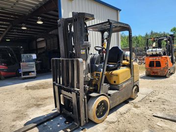 A yellow CAT forklift parked outside a warehouse under clear blue sky.