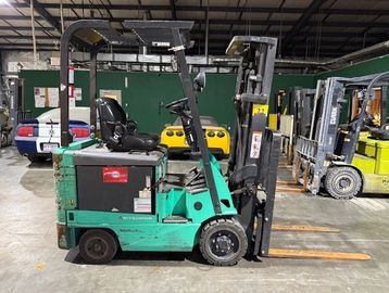 Green forklift parked inside a warehouse with other forklifts and vehicles.