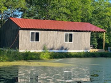 Wooden cabin by a pond with trees.