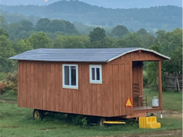 Wooden tiny house on wheels in a grassy field.