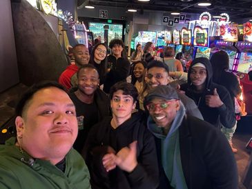 Group of friends smiling and posing for a selfie in a lively arcade.