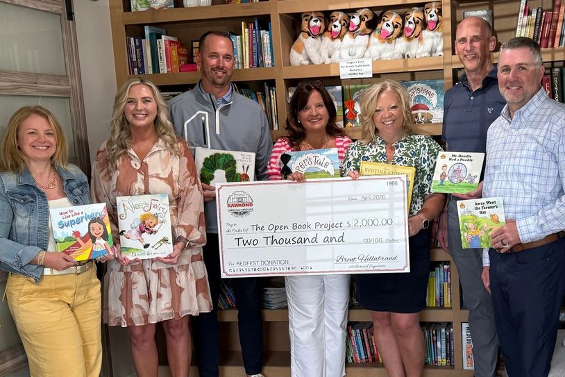 Group holding books and a large donation check for The Open Book Project.