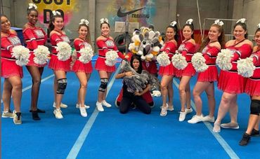 Cheerleaders in red uniforms posing with mascot on blue gym floor.