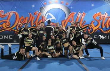 Cheerleading team in black and gold uniforms posing on blue mat.