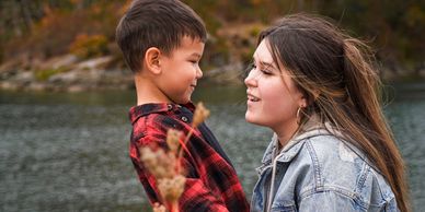 Woman crouching by a lake, smiling at a young boy in a red plaid shirt. Photography by Lucy L Massie, Serene Scene Studio - Duncan, BC.