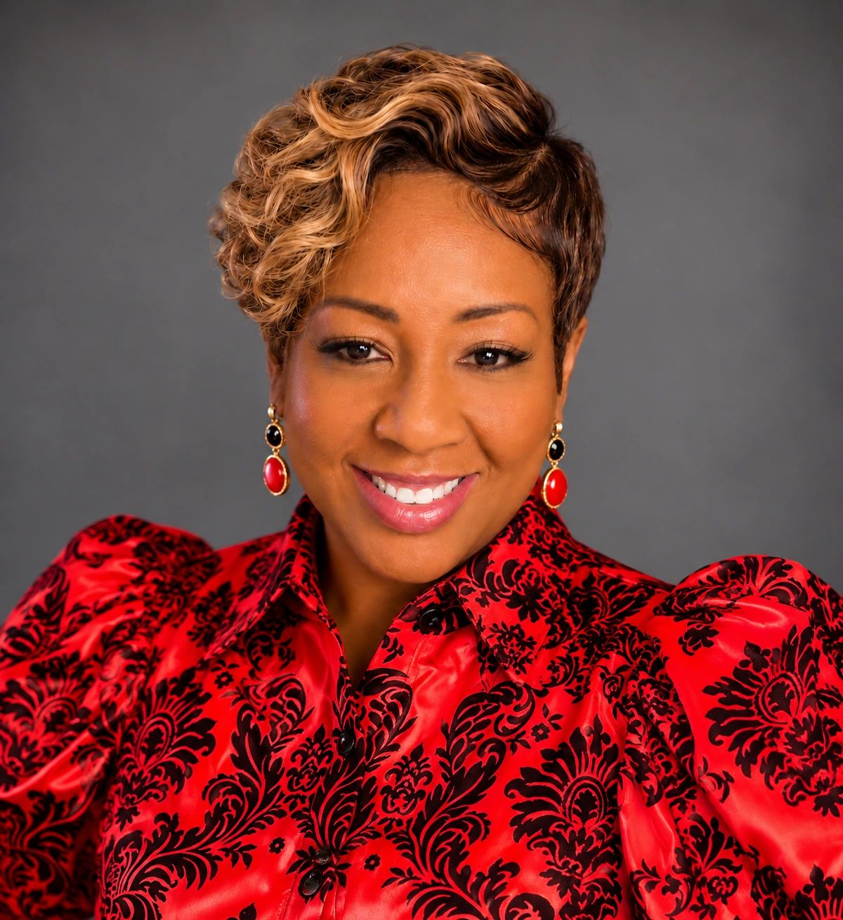 Confident woman with styled hair in a red and black patterned blouse.