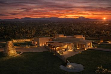 Casa moderna iluminada al atardecer con fondo montañoso.