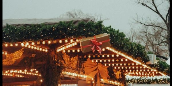 Festive holiday market stall adorned with lights, greenery, and a gift box.