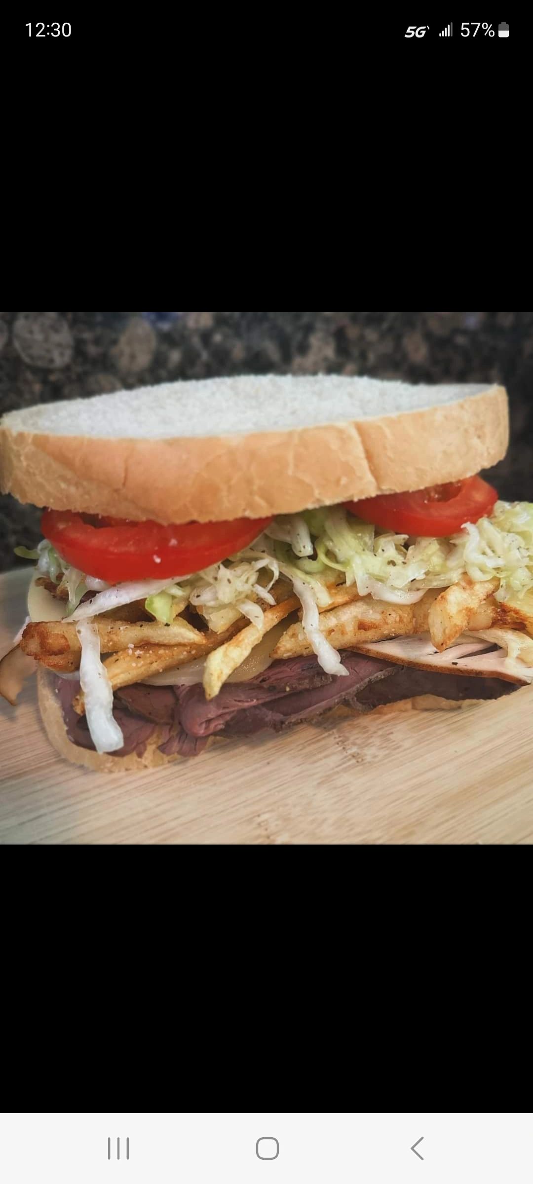 Homemade sandwich with lettuce, tomato, fries, and deli meats on white bread.
