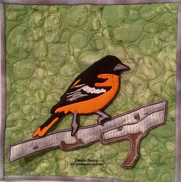 Baltimore Oriole tiny quilt on green background.