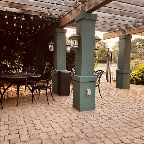 Outdoor patio with wrought iron furniture and string lights under wooden pergola.