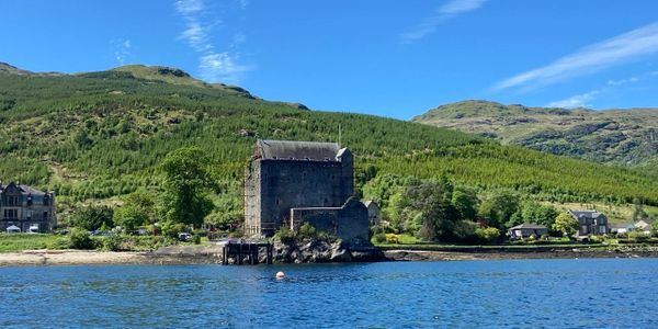 Ancient stone castle by a calm blue lake with green hills in the background.