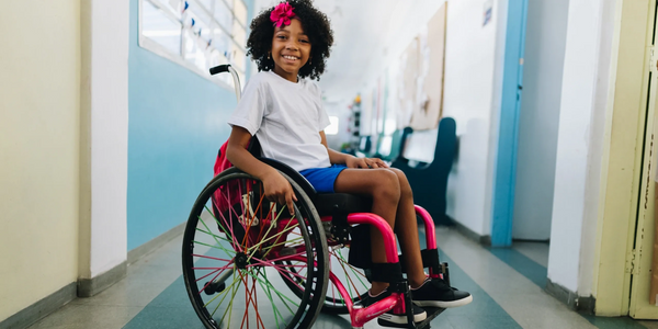 Smiling young girl in a colorful wheelchair in a bright hallway with cerebral palsy.
