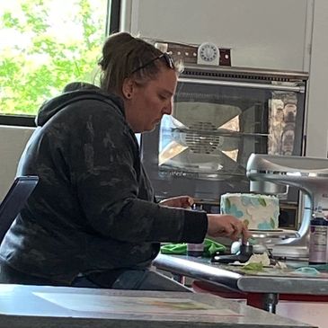 A woman decorating a cake with various icing supplies on the table.