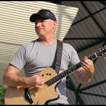 Man playing guitar outdoors with a smile.