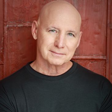 Smiling bald man with blue eyes in front of a red wall.