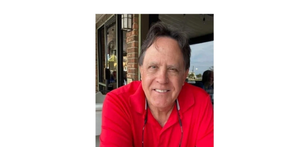 Smiling man in a red shirt sitting outdoors at a café.