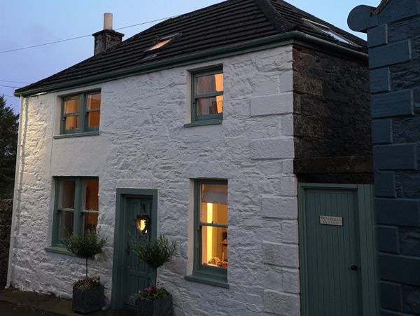 Cozy stone cottage with green trim and warm interior lights at dusk.