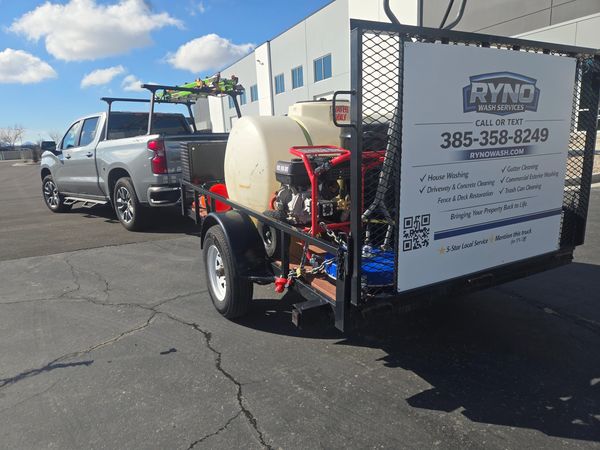 A pickup truck towing a trailer with a water tank and pressure washer for cleaning services.