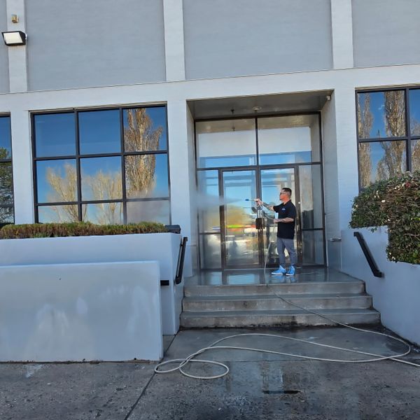 Person pressure washing a building entrance with hose on concrete steps.