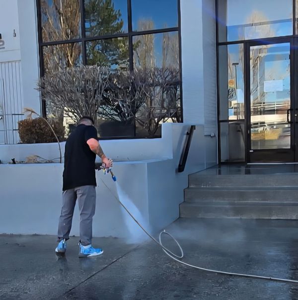 Man pressure washing a concrete sidewalk outside a building.