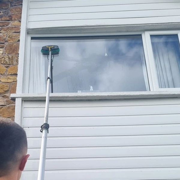 Person cleaning a high window with an extended brush.