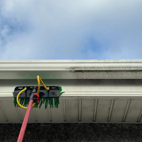 Cleaning a dirty gutter edge with a brush and hose.