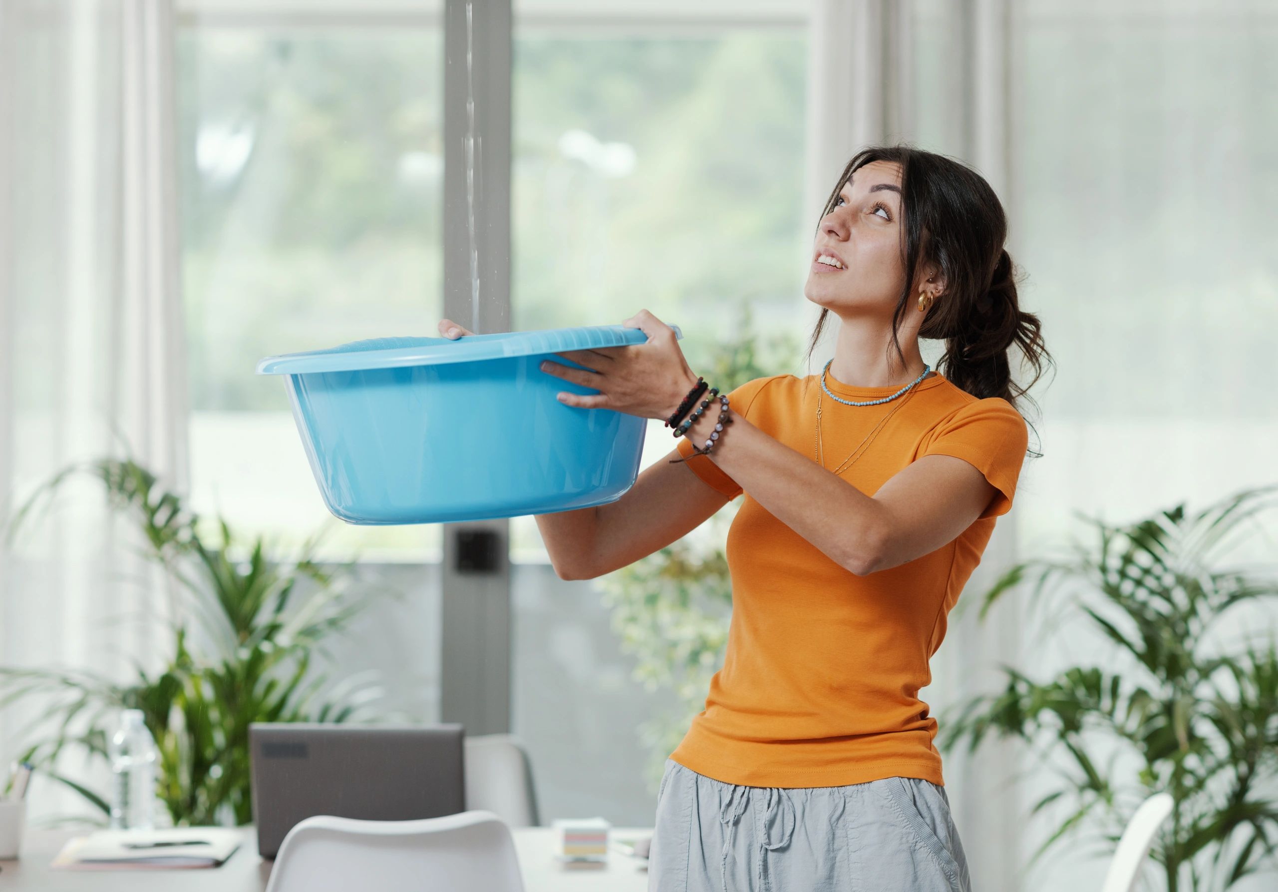 Woman holding a blue basin indoors, looking up.