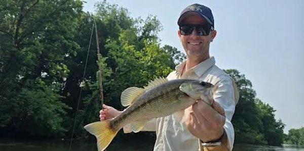 Man proudly holds a large fish he caught while fishing in a river.