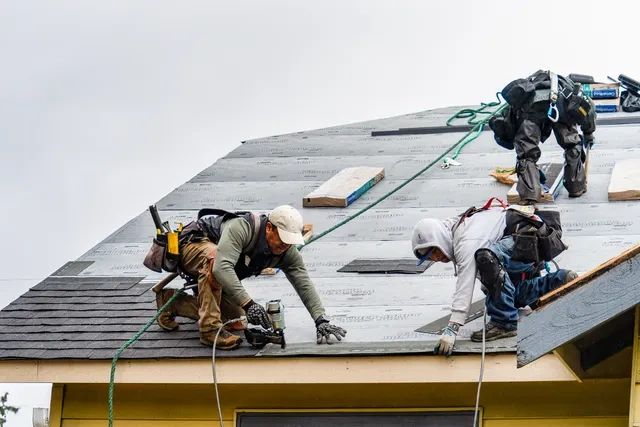 Two construction workers installing a roof on a house.