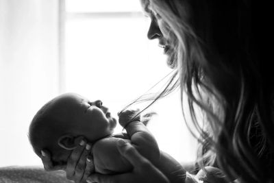 Mother lovingly holds and gazes at her newborn baby in soft light.