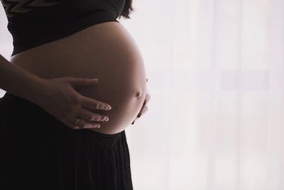 Pregnant woman gently holding her belly in soft natural light.