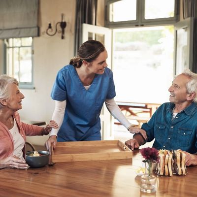 Caregiver interacts warmly with elderly couple at dining table.