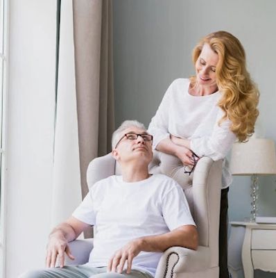 A woman smiling at a seated man in a cozy room.