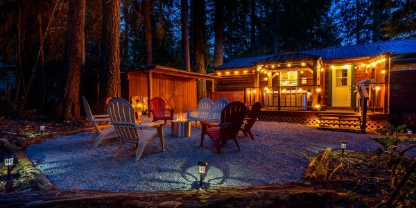 Cozy outdoor seating with fire pit and string lights around a cabin at night.