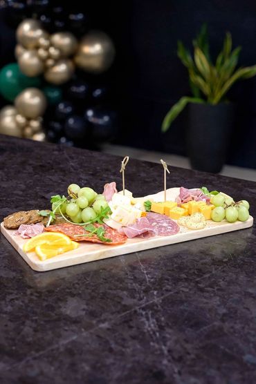 A charcuterie board with cheese, meats, grapes, crackers, and orange slices.