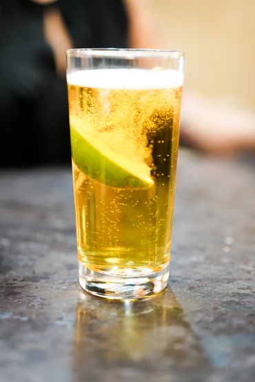 Glass of beer with a lime wedge on a table.