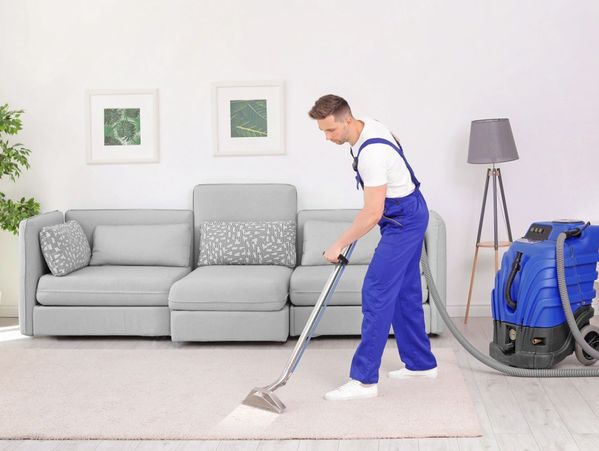 Male worker removing dirt from carpet with professional vacuum cleaner indoors