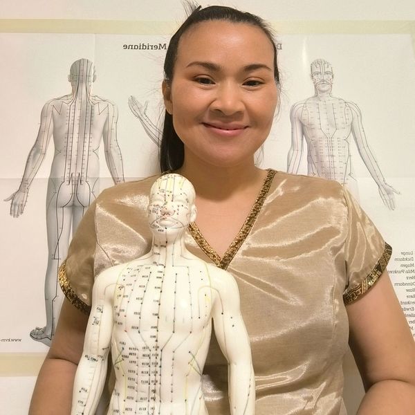 Frau mit Akupunkturmodell und Diagrammen im Hintergrund.