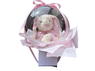A plush bunny inside a transparent balloon with pink ribbon and wrapping.