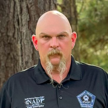 Serious man with bald head and long goatee wearing a black NADP shirt.