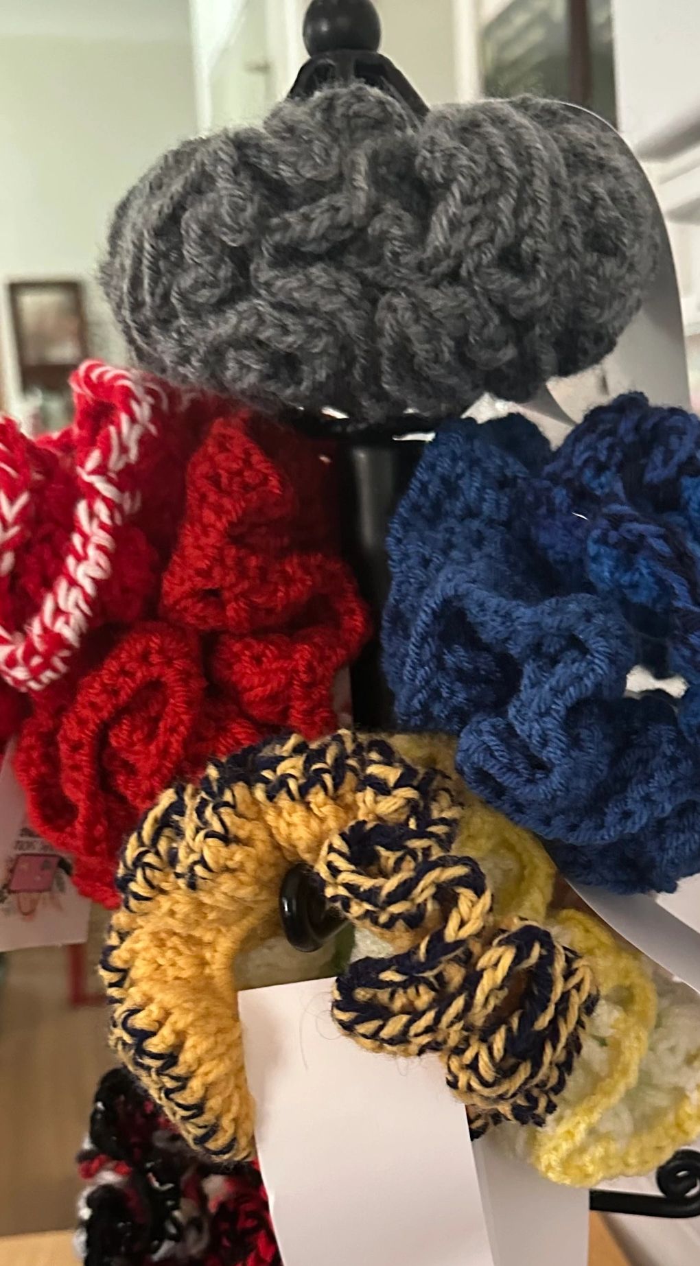 Colorful crocheted scrunchies displayed on a black stand.