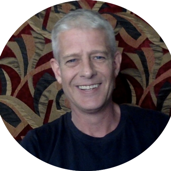 Smiling man with gray hair in front of a patterned background.