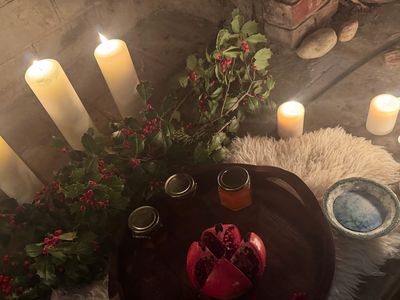 Cozy setting with lit candles, greenery, honey jars, and pomegranate on a wooden tray.